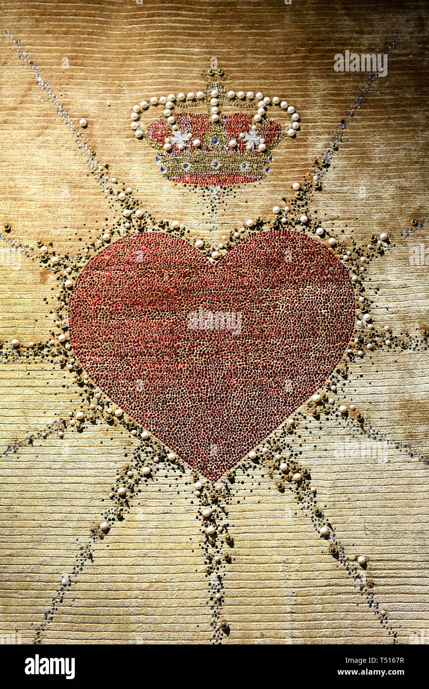Gestickte Herzen und heraldische Krone auf Wandteppich mit ausgehenden Strahlen auf beige Stoff farbig Stockfoto