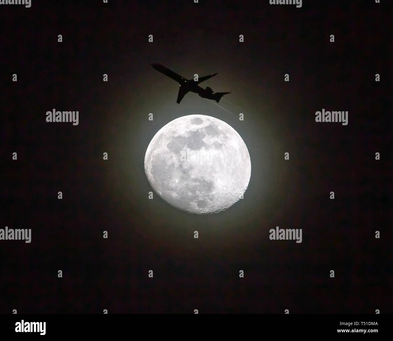 Ein Verkehrsflugzeug in niedriger Höhe passiert einen Vollmond in der Nacht. Stockfoto