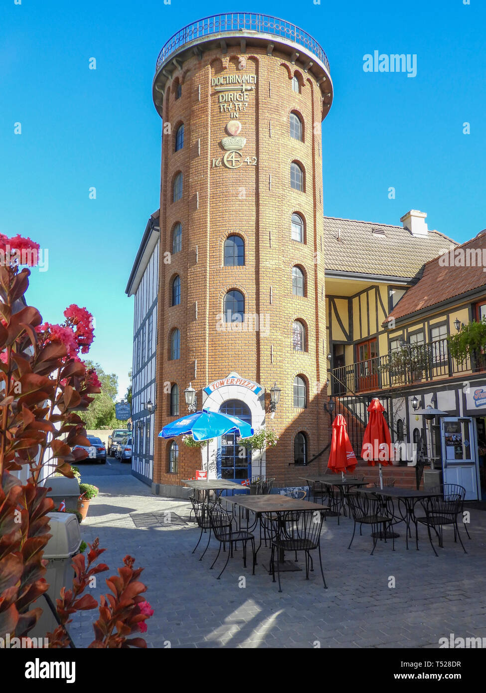 Terrasse mit Tischen und Stühlen, Essen businessess und runde hohes Ziegelgebäude mit Bogenfenstern erreicht für den blauen Himmel. Stockfoto