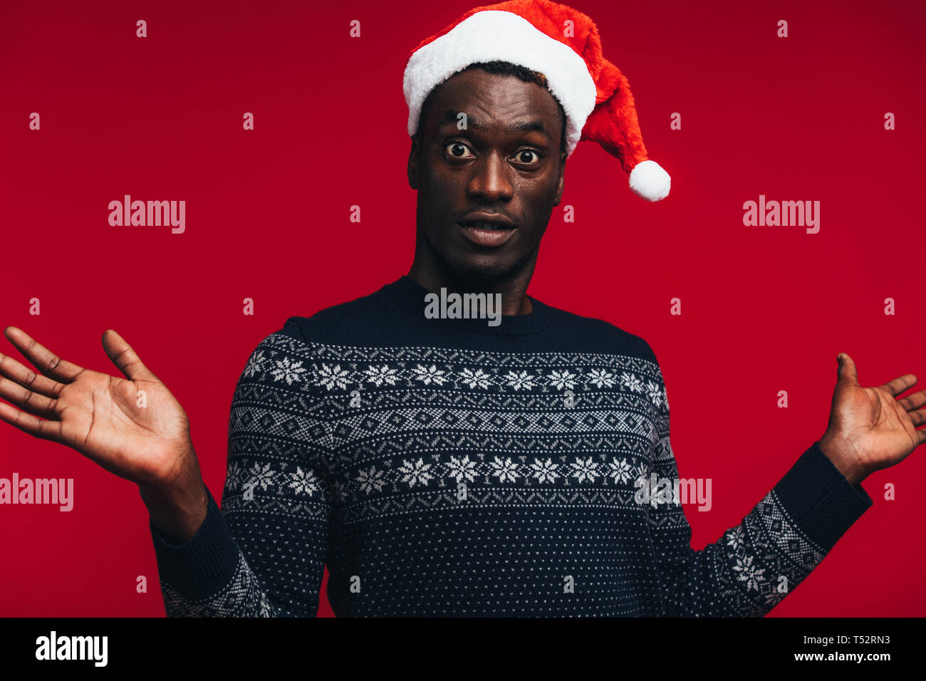 Afrikanische amerikanische Mann mit Santa hat über den roten Hintergrund überrascht. Überrascht leer Kerl auf Kamera. Stockfoto
