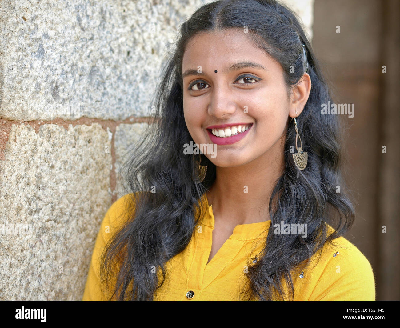 Schöne indische Mädchen mit stilvollen Ohrringe trägt einen gelben Kleid und Lächeln für die Kamera. Stockfoto