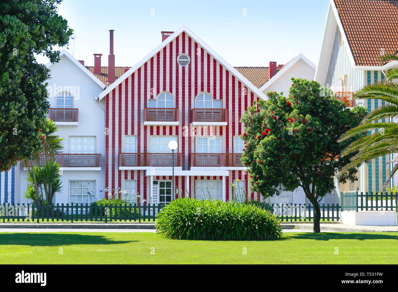 Gemütliche bunt gestreiften Haus mit roten und weißen Streifen in der Landschaft, Rasen und Blühender Baum mit roten Blüten. Costa Nova, Portugal. Stockfoto