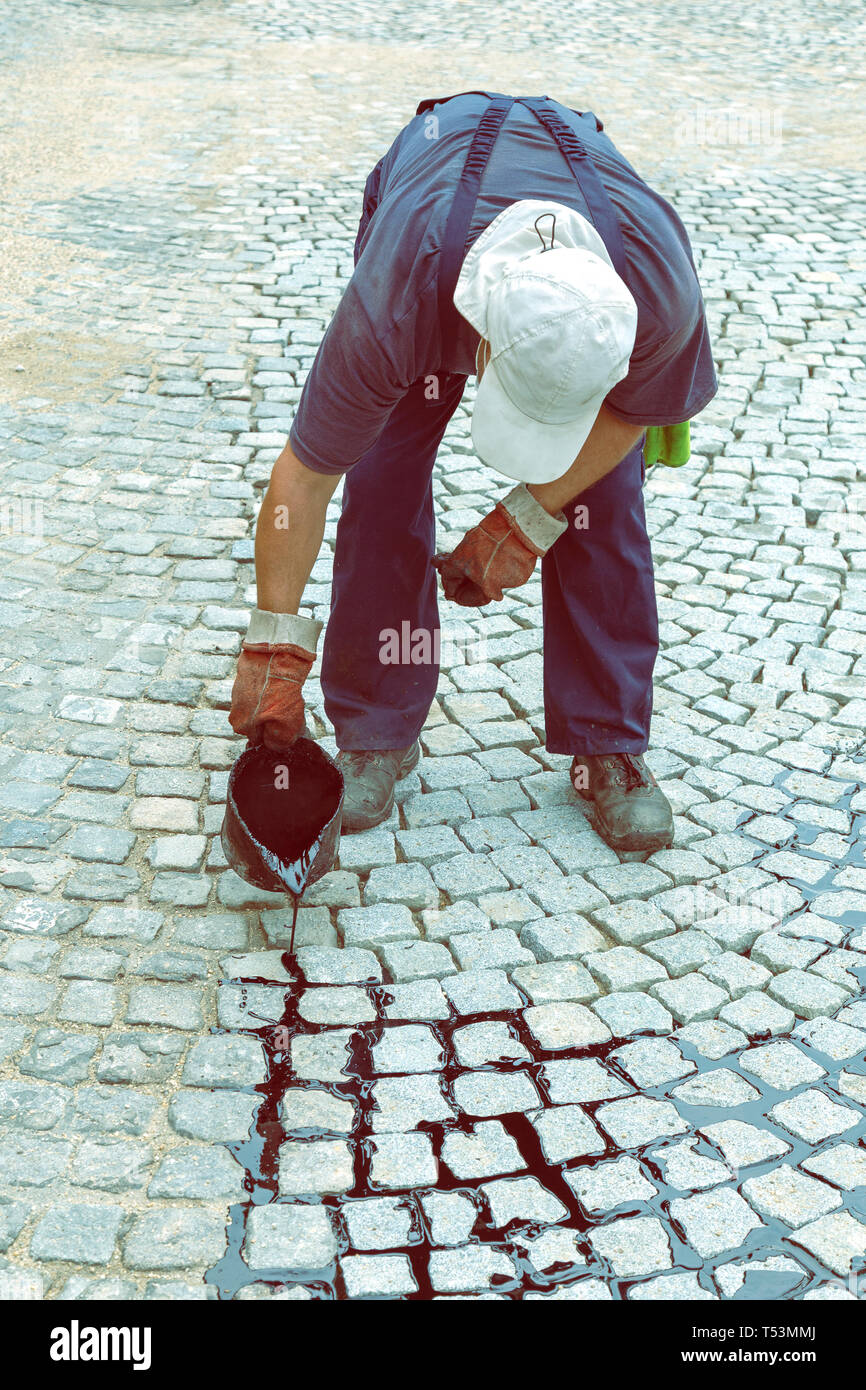 Arbeiter gießt Bitumen der gemeinsamen von der Straße zu übernehmen. Traditionelle pitch Verfugung für gepflasterte Auffahrt. Verwenden des Pitch Schaufel, Verbreitung von flüssigem Teer zu gelten. Stockfoto