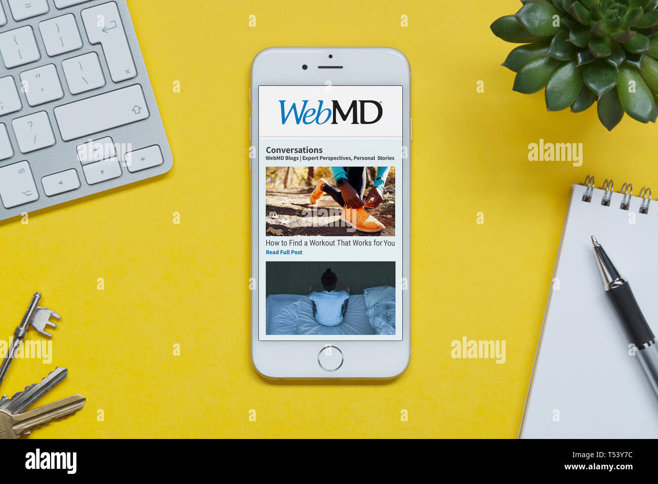 Ein iPhone zeigt die WebMD website ruht auf einem gelben Hintergrund Tabelle mit einer Tastatur, Tasten, Notepad und Anlage (nur redaktionelle Nutzung). Stockfoto