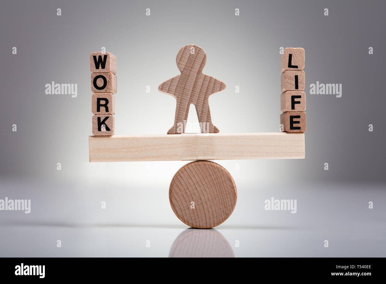 Menschliche Figur, den Ausgleich zwischen Arbeit und Leben auf hölzernen Wippe gegen grauer Hintergrund Stockfoto