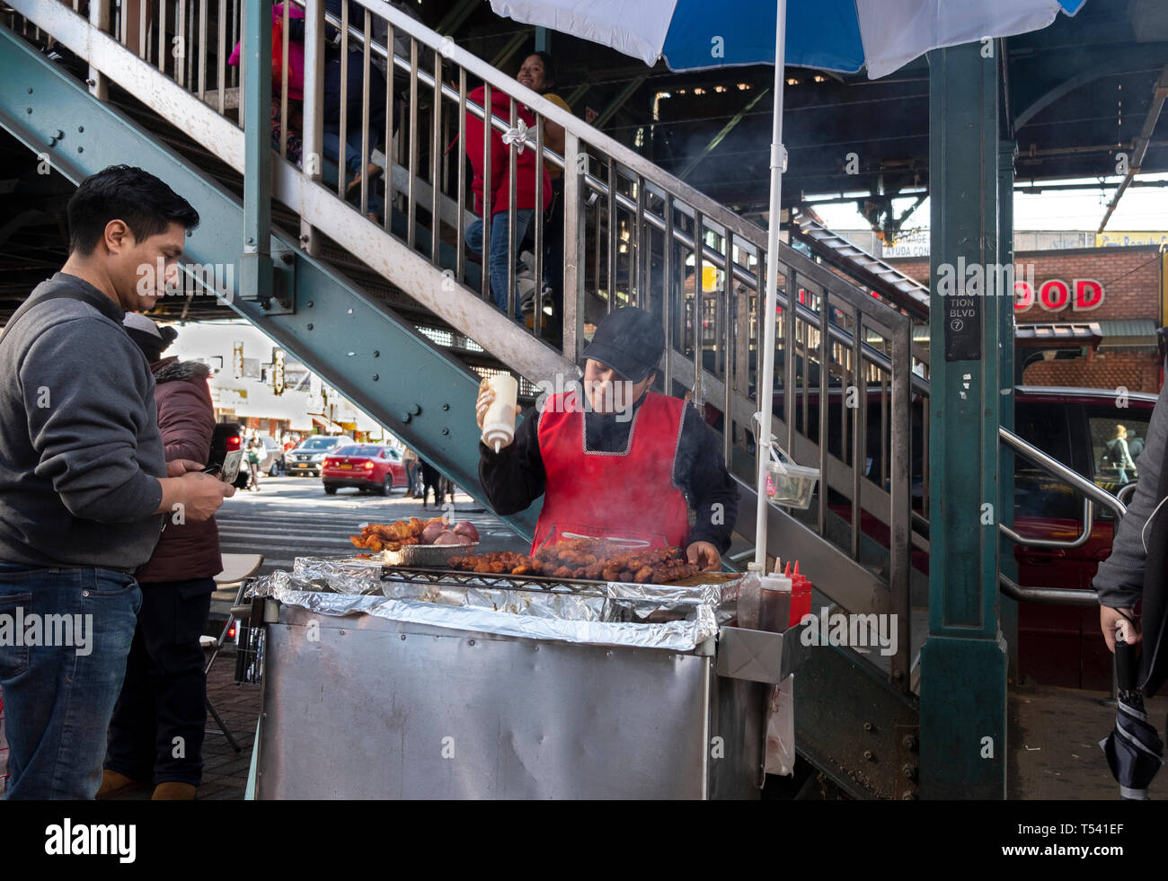 Eine Südamerikanische Frau verkaufen Gegrilltes Fleisch aus einem Stand unterhalb der erhöhten und U-Bahn. In der Corona, Queens, NYC Stockfoto
