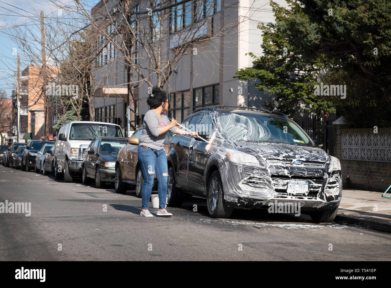 Eine Frau ihr SUV Waschen mit Wasser und Seife in einer Seitenstraße in der Corona, Queens, New York City Stockfoto