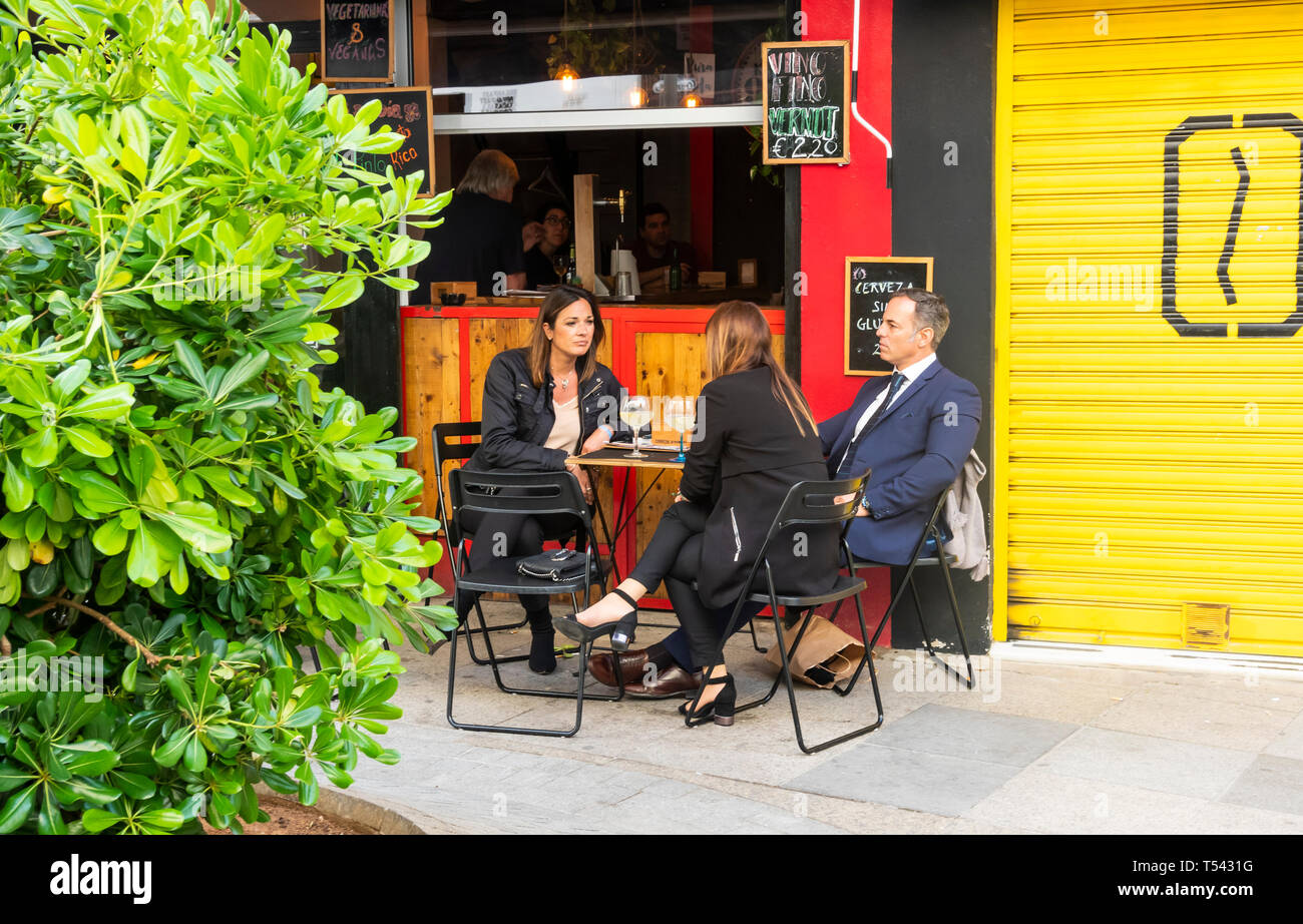 Drei Freunde teilen sich einen Drink im Freien und ein Gespräch in einem Café in Sevilla Stockfoto