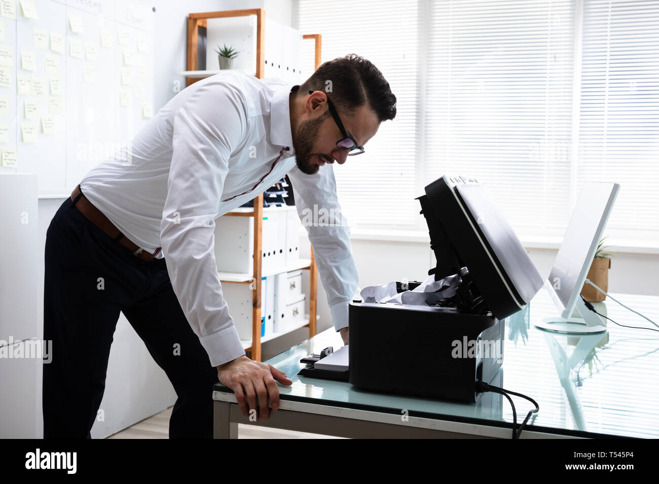 Junge gereizter Geschäftsmann auf der Suche nach Drucker im Büro Stockfoto