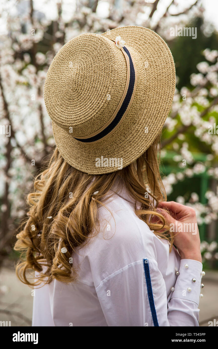 Eine junge schöne Kaukasische Mädchen in einem canote Hut steht mit dem Rücken unter den weiß blühenden Bäumen. Frühling Stockfoto