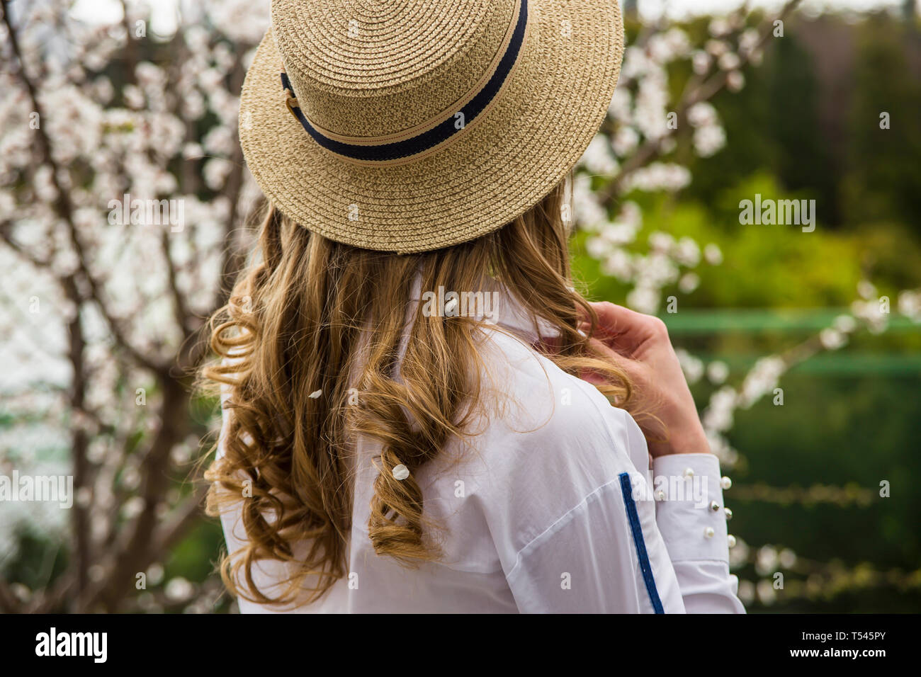 Eine junge schöne Kaukasische Mädchen in einem canote Hut steht mit dem Rücken unter den weiß blühenden Bäumen. Frühling Stockfoto