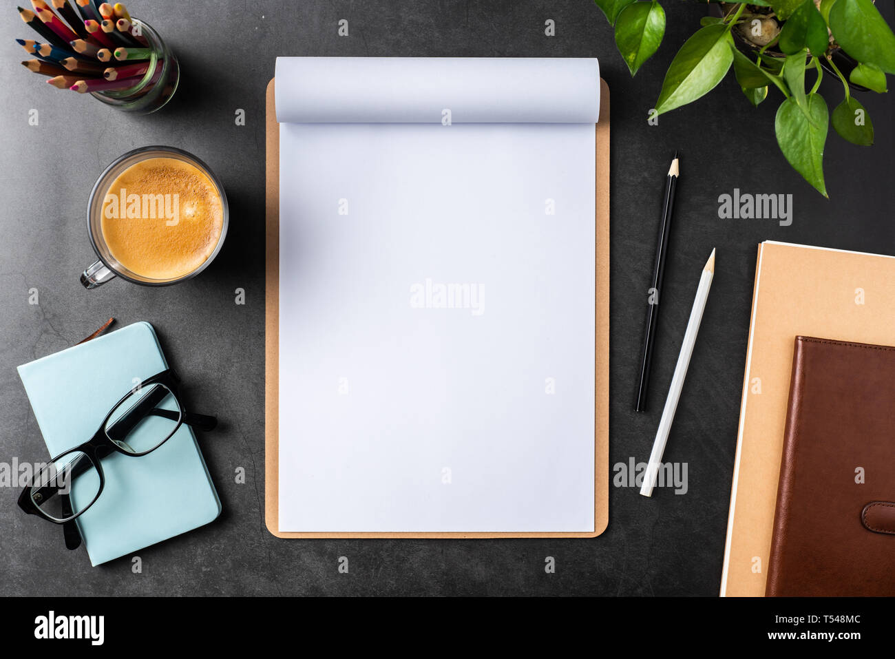 Designkonzept - Ansicht von oben auf weißem A4-Papier mit braunen Zwischenablage umgedreht, Topfpflanze, Gläser, Kaffee, Bleistift auf schwarzen Hintergrund für mockup. real p Stockfoto