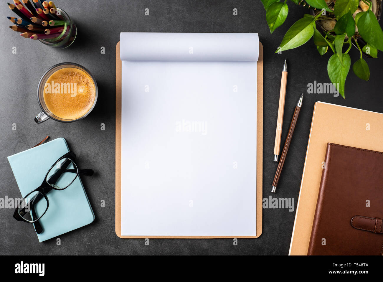 Designkonzept - Ansicht von oben auf weißem A4-Papier mit braunen Zwischenablage umgedreht, Topfpflanze, Gläser, Kaffee, Bleistift auf schwarzen Hintergrund für mockup. real p Stockfoto