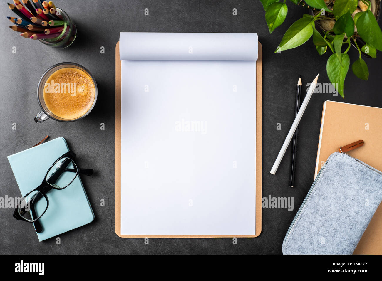 Designkonzept - Ansicht von oben auf weißem A4-Papier mit braunen Zwischenablage umgedreht, Topfpflanze, Gläser, Kaffee, Bleistift caes auf schwarzen Hintergrund für mockup. r Stockfoto