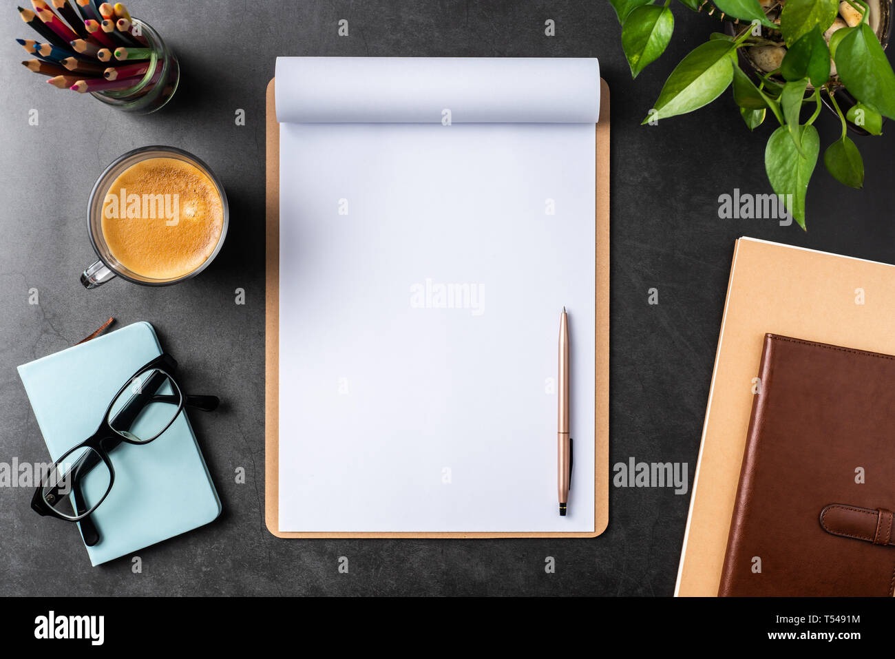Designkonzept - Ansicht von oben auf weißem A4-Papier mit braunen Zwischenablage umgedreht, Topfpflanze, Gläser, Kaffee, Bleistift auf schwarzen Hintergrund für mockup. real p Stockfoto