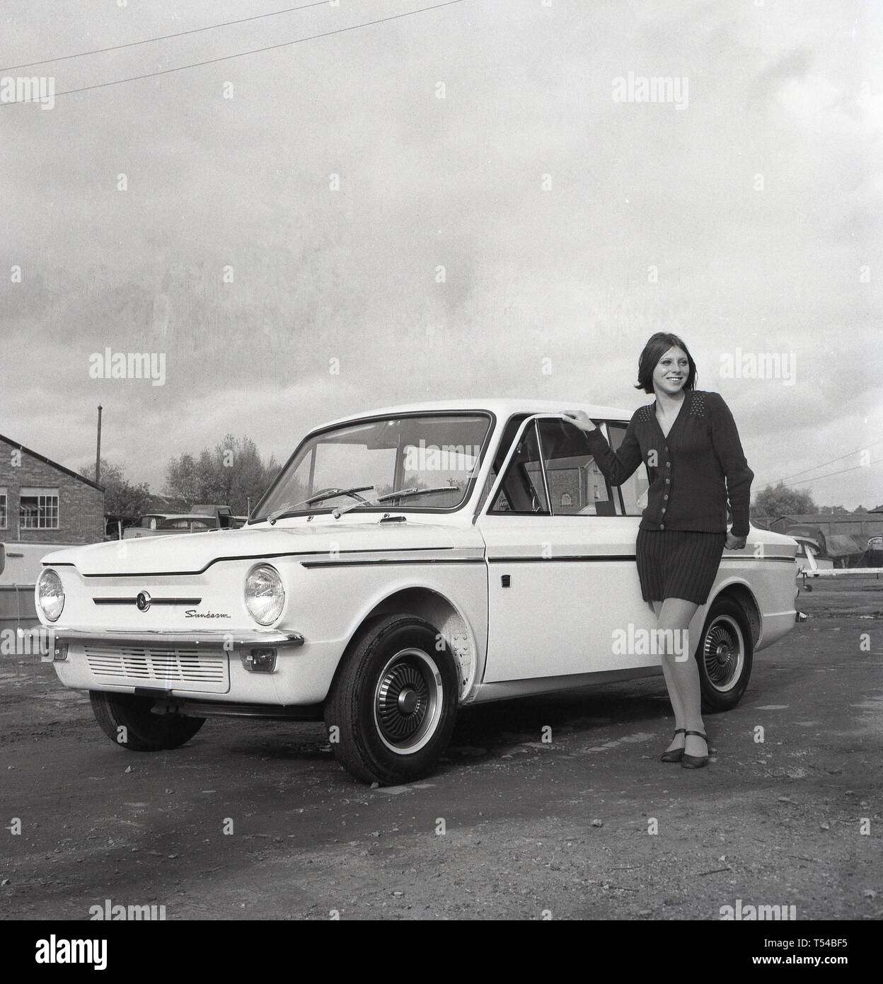 1967, historische, junge Dame trägt eine Wollene Strickjacke und Rock neben einem Sonnenstrahl Sport Auto posiert, die sportliche Version des berühmten kleinen Auto, den HIllman Imp. Die Hillman Imp war ein kleines Auto mit Rootes Group und ihrer Nachfolger Chrysler Europa von 1963 bis 1976 war die Wettbewerber in das kleine Auto Kategorie in die Mini gemacht. Stockfoto
