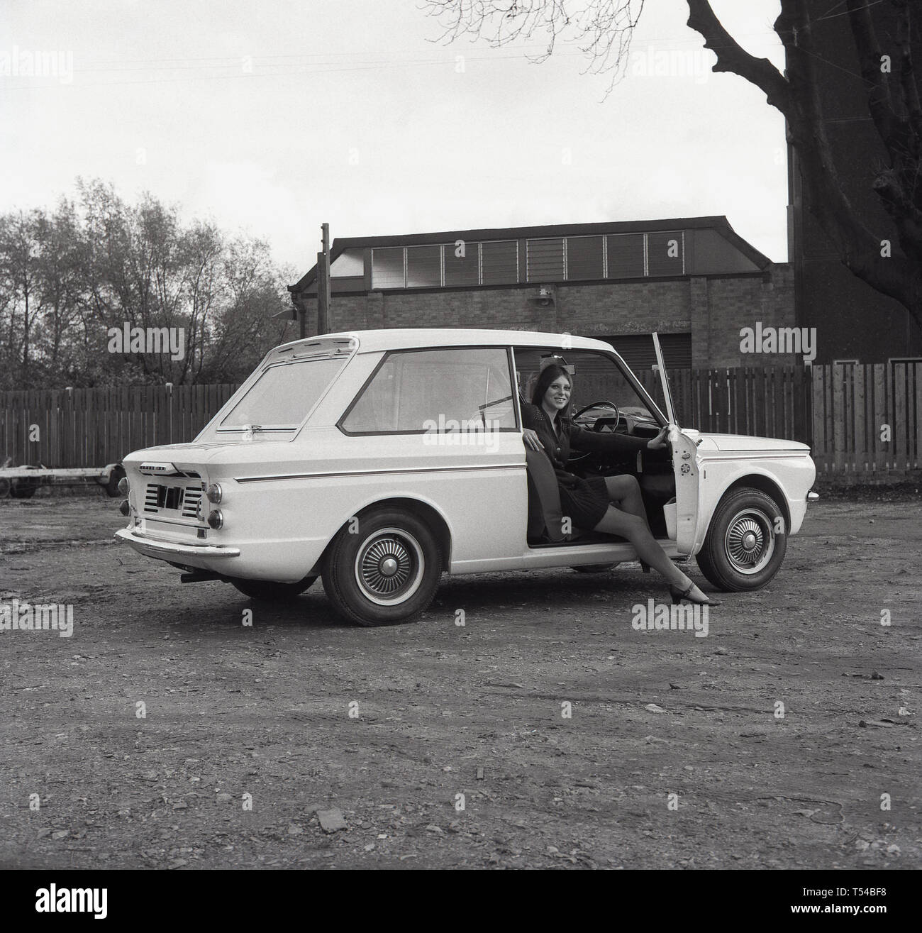 1967, historische, junge Dame trägt eine Wollene Strickjacke und Rock sitzt auf dem Fahrersitz eines Sunbeam Sport Auto, die zwei - Tür Sport Version des berühmten kleinen Auto, den HIllman Imp. Die Hillman Imp war ein kleines Auto mit Rootes Group und ihrer Nachfolger Chrysler Europa von 1963 bis 1976 war die Wettbewerber in das kleine Auto Kategorie in die Mini gemacht. Stockfoto