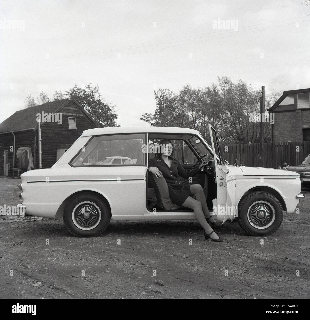 1967, historische, junge Dame trägt eine Wollene Strickjacke und Rock sitzt auf dem Fahrersitz eines Sunbeam Sport Auto, die sportliche Version des berühmten kleinen Auto, den HIllman Imp. Die Hillman Imp war ein kleines Auto mit Rootes Group und ihrer Nachfolger Chrysler Europa von 1963 bis 1976 war die Wettbewerber in das kleine Auto Kategorie in die Mini gemacht. Stockfoto