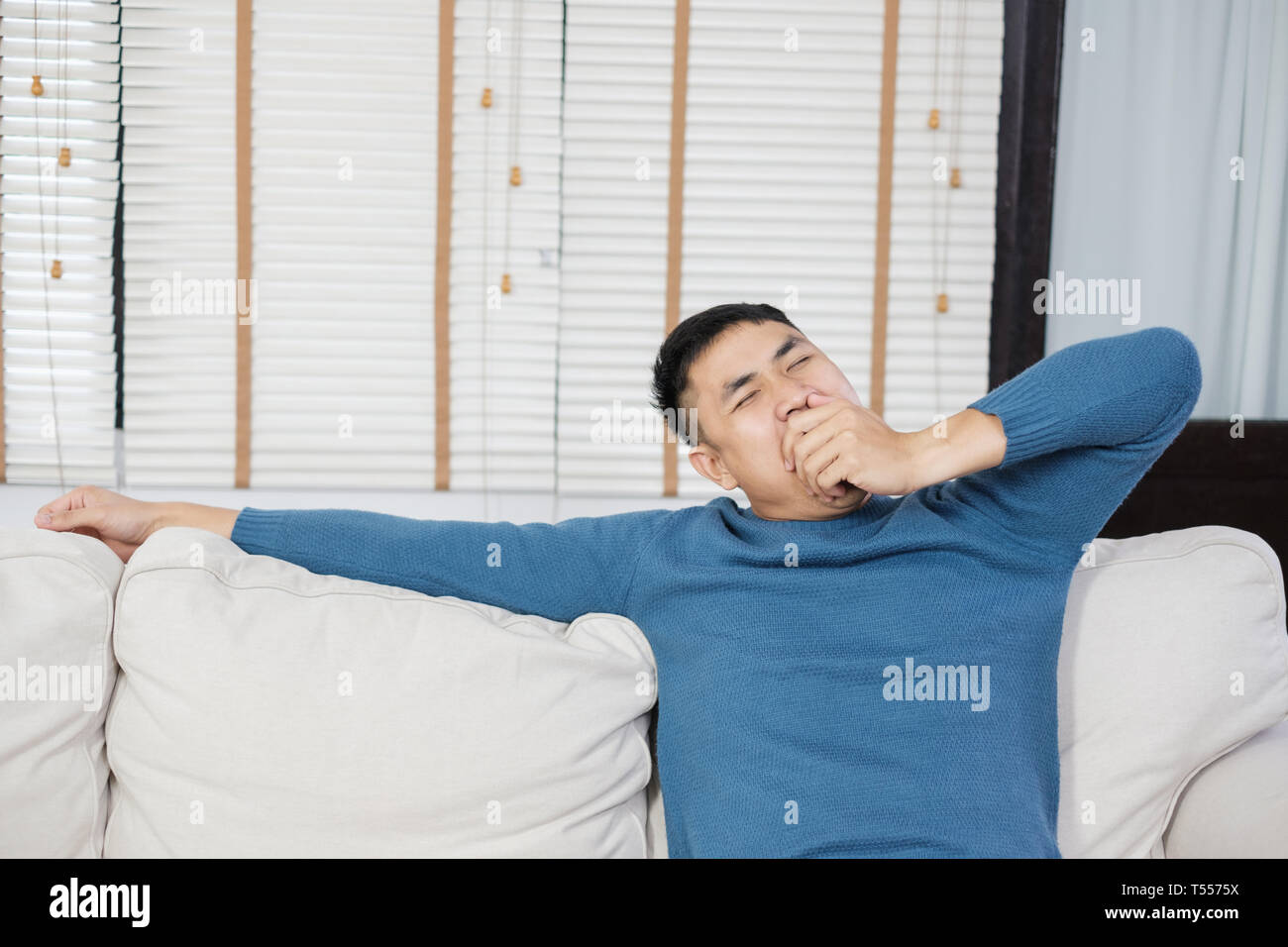 Asiatischer mann Standortwahl auf Sofa und Gähnen, wenn sie Ende Kasten, neues Haus mit Müdigkeit Stockfoto