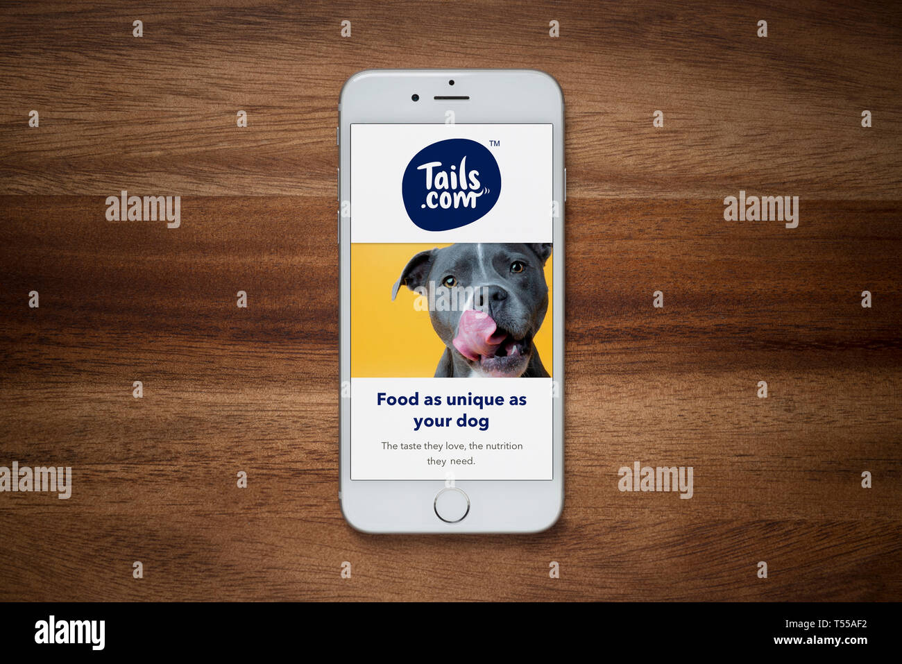 Ein iPhone mit der Tails.com Website beruht auf einem einfachen Holztisch (nur redaktionelle Nutzung). Stockfoto