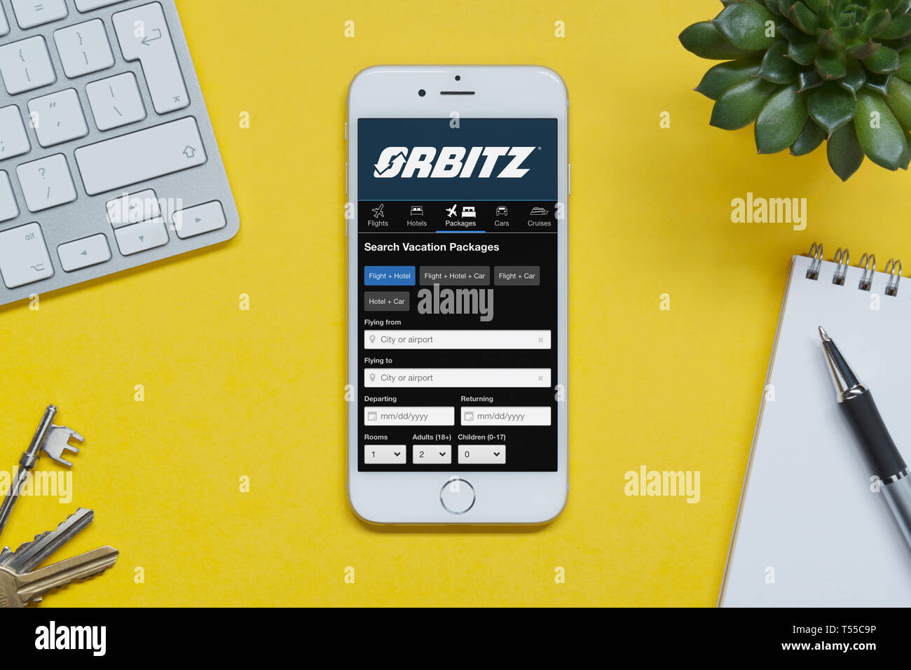 Ein iPhone zeigt die Orbitz website ruht auf einem gelben Hintergrund Tabelle mit einer Tastatur, Tasten, Notepad und Anlage (nur redaktionelle Nutzung). Stockfoto