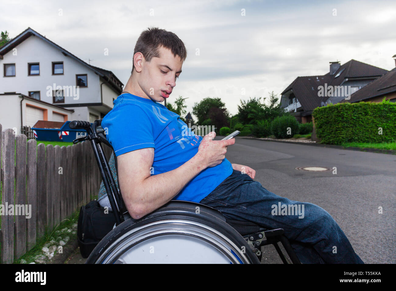 Behinderten Jungen mit Smartphone warten auf den Schulbus Stockfoto