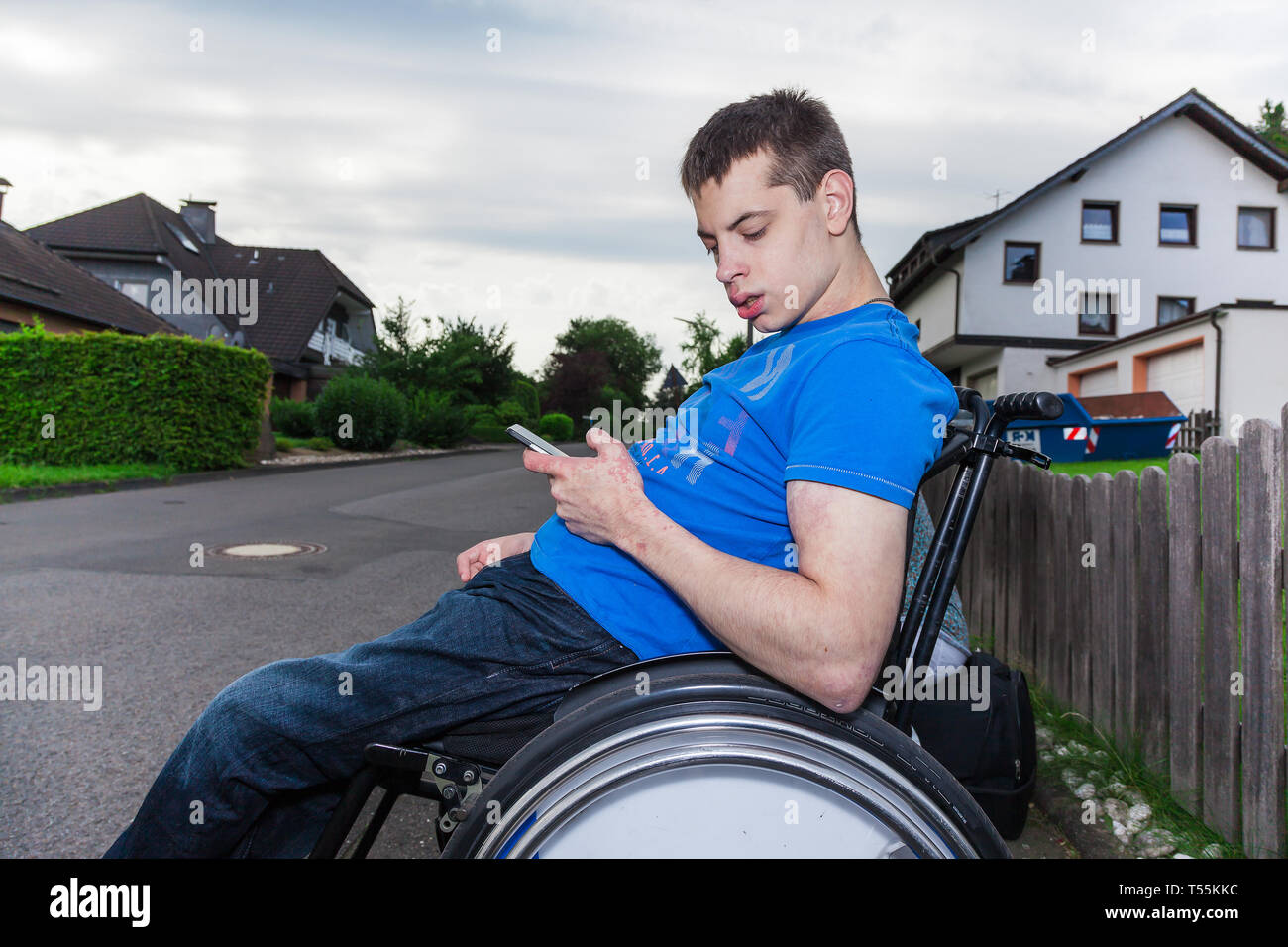 Behinderten Jungen mit Smartphone warten auf den Schulbus Stockfoto
