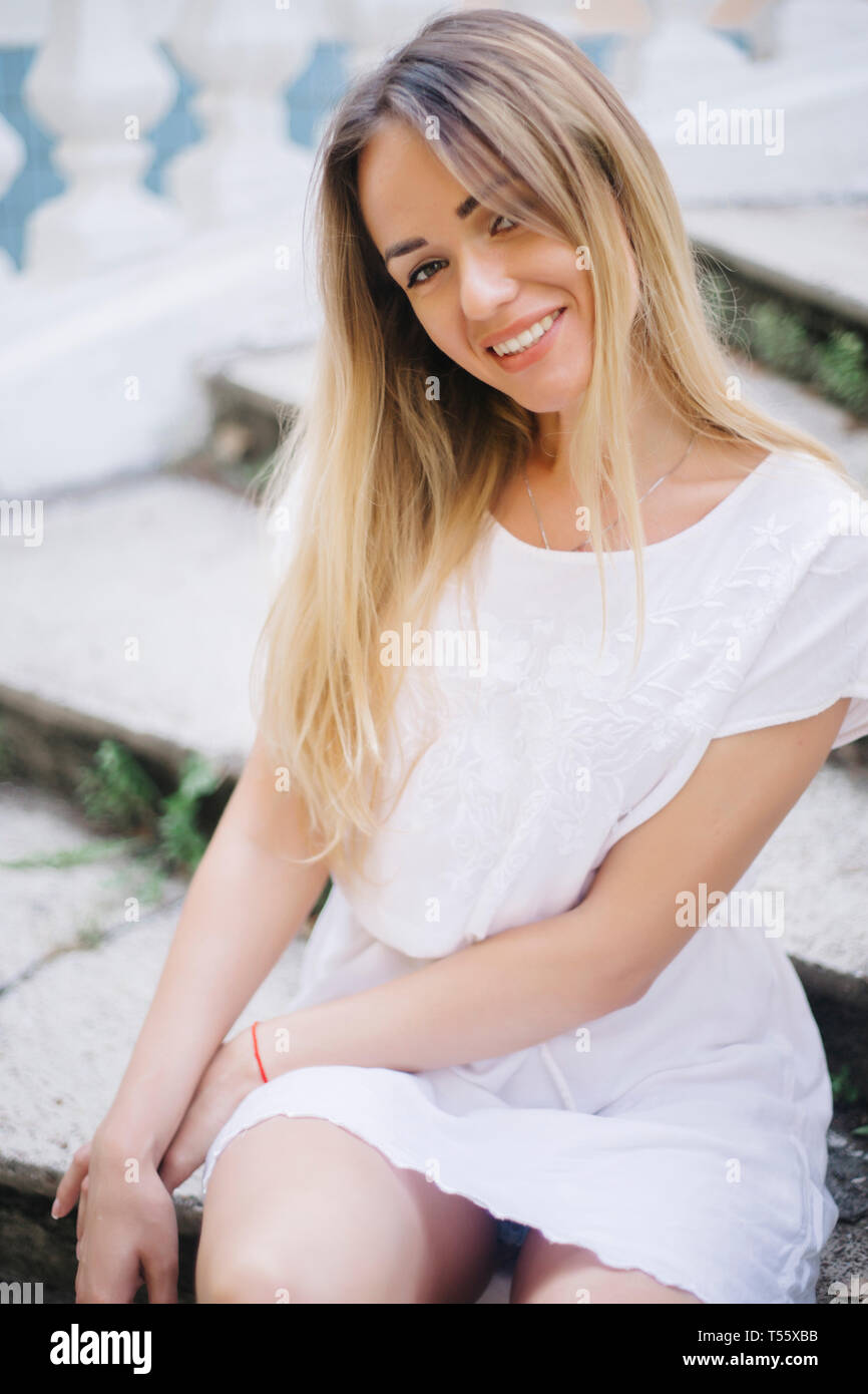 Junge Frau in weißem Kleid sitzt auf Schritte Stockfoto