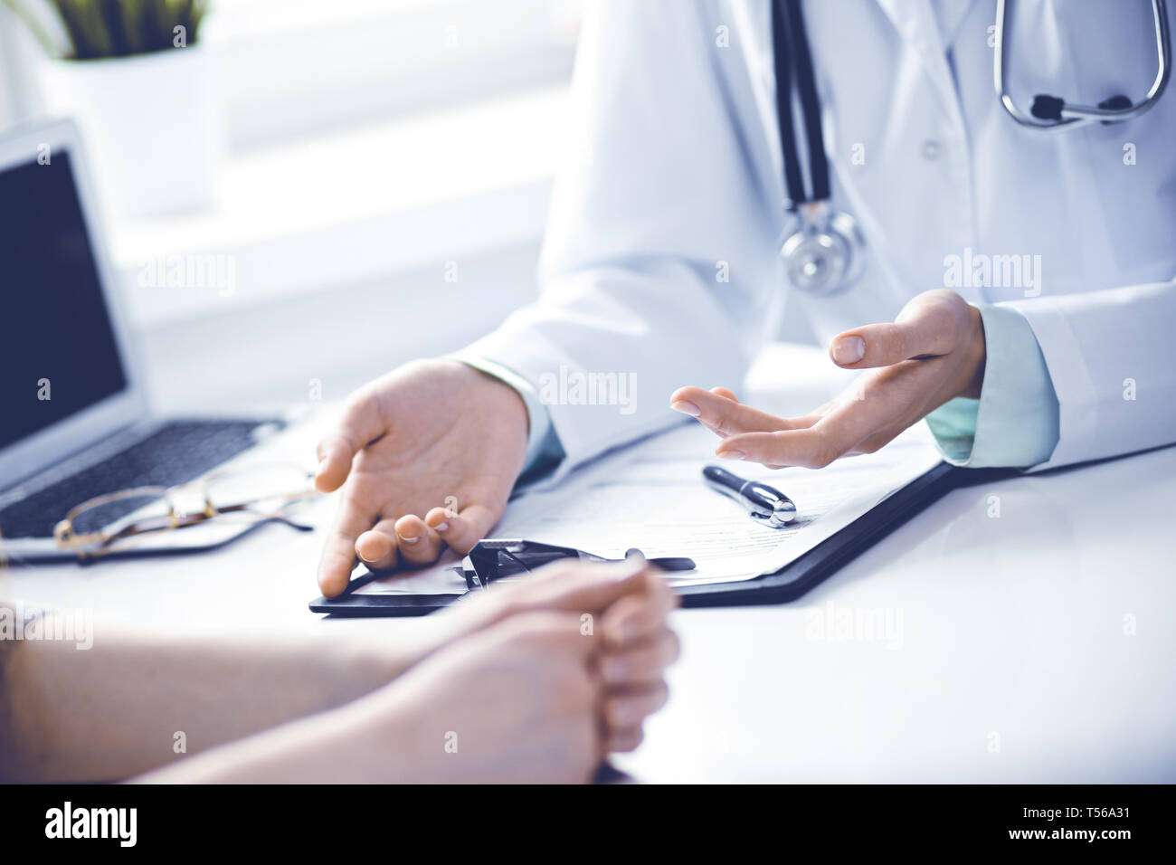 Arzt und Patientin am Schreibtisch sitzt und spricht in der Klinik in der Nähe der Fenster