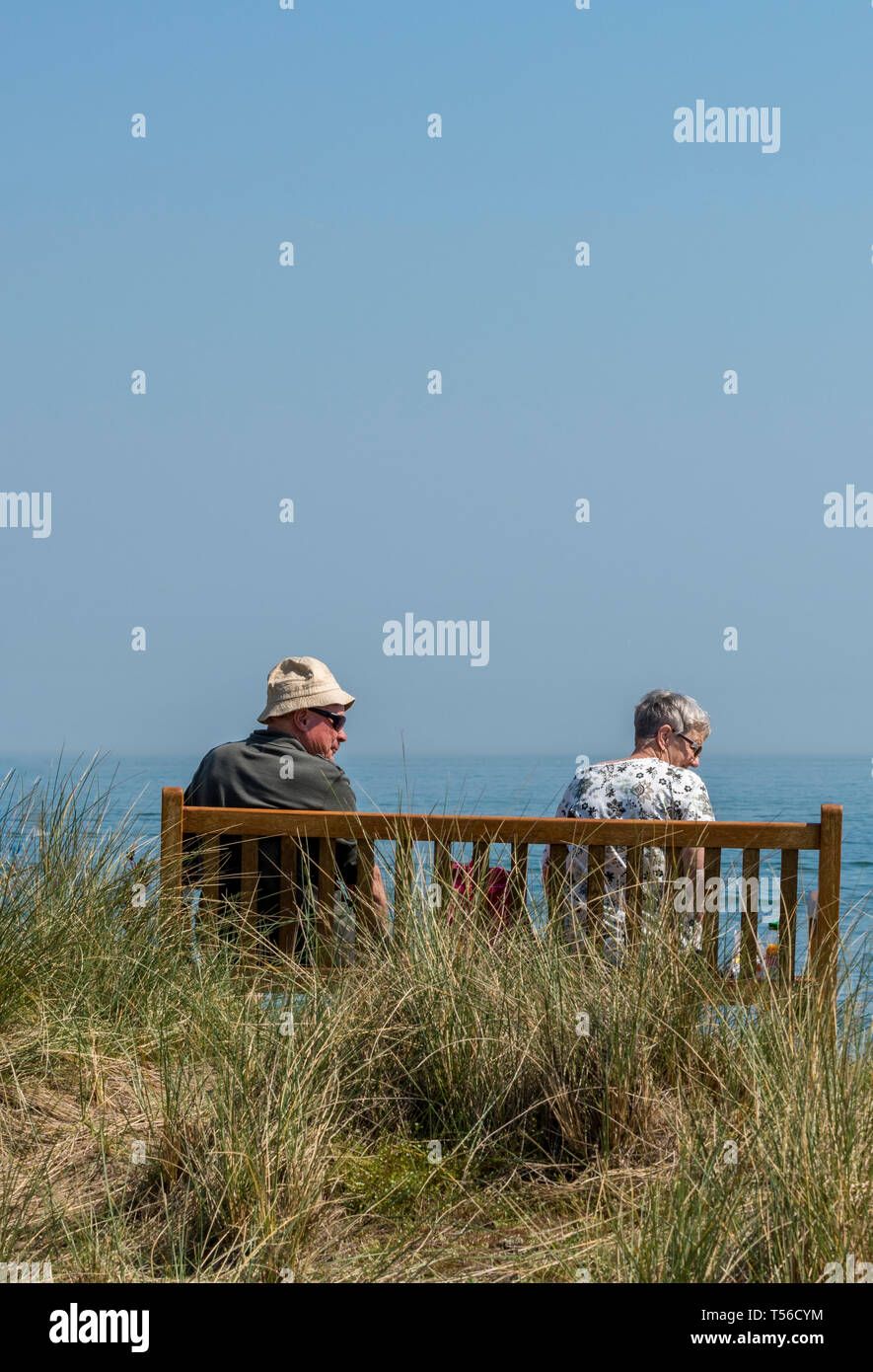 Ein älteres Paar auf einer Bank sitzen am Meer an einem warmen sonnigen Tag im Sommer im Urlaub auf der Insel Wight. Stockfoto