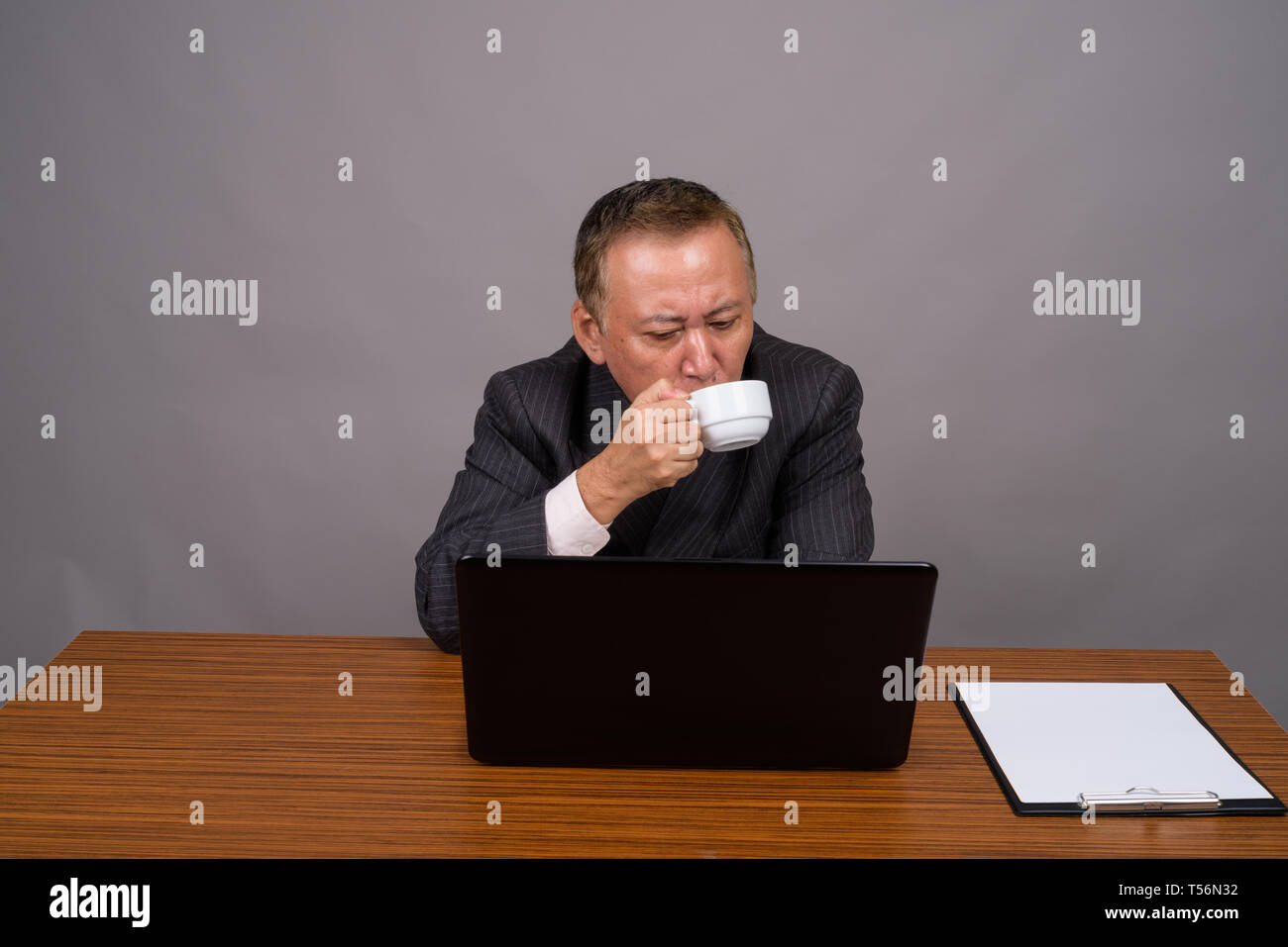 Reifen asiatische Geschäftsmann sitzen mit hölzernen Tisch gegen Grau Stockfoto