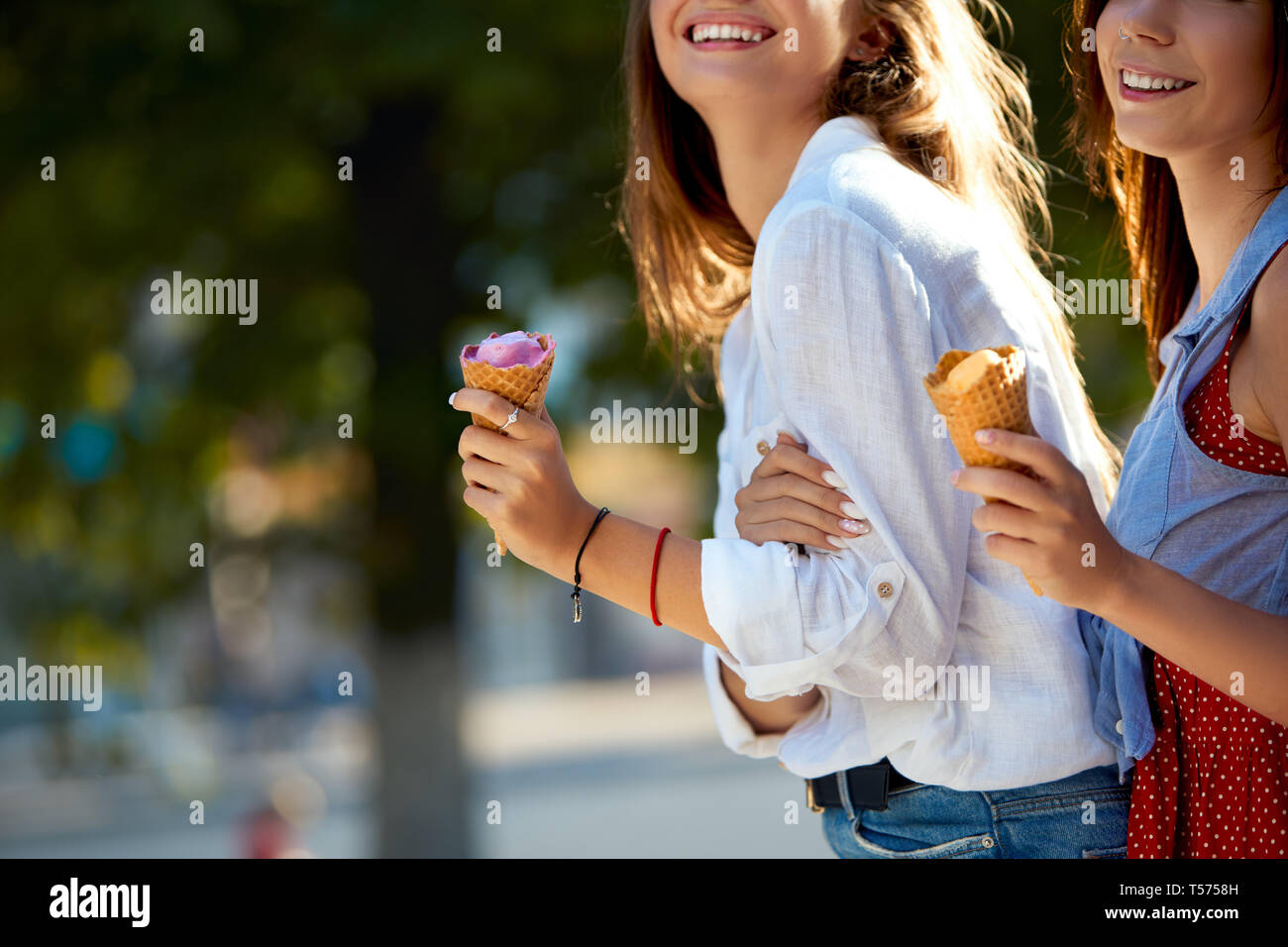 Nahaufnahme von Eistüten in der Hand einer Frau, die mit ihrem Freund. Zwei junge Frauen im Freien essen Eis an einem sonnigen Tag. Isolierte Sicht, Stockfoto