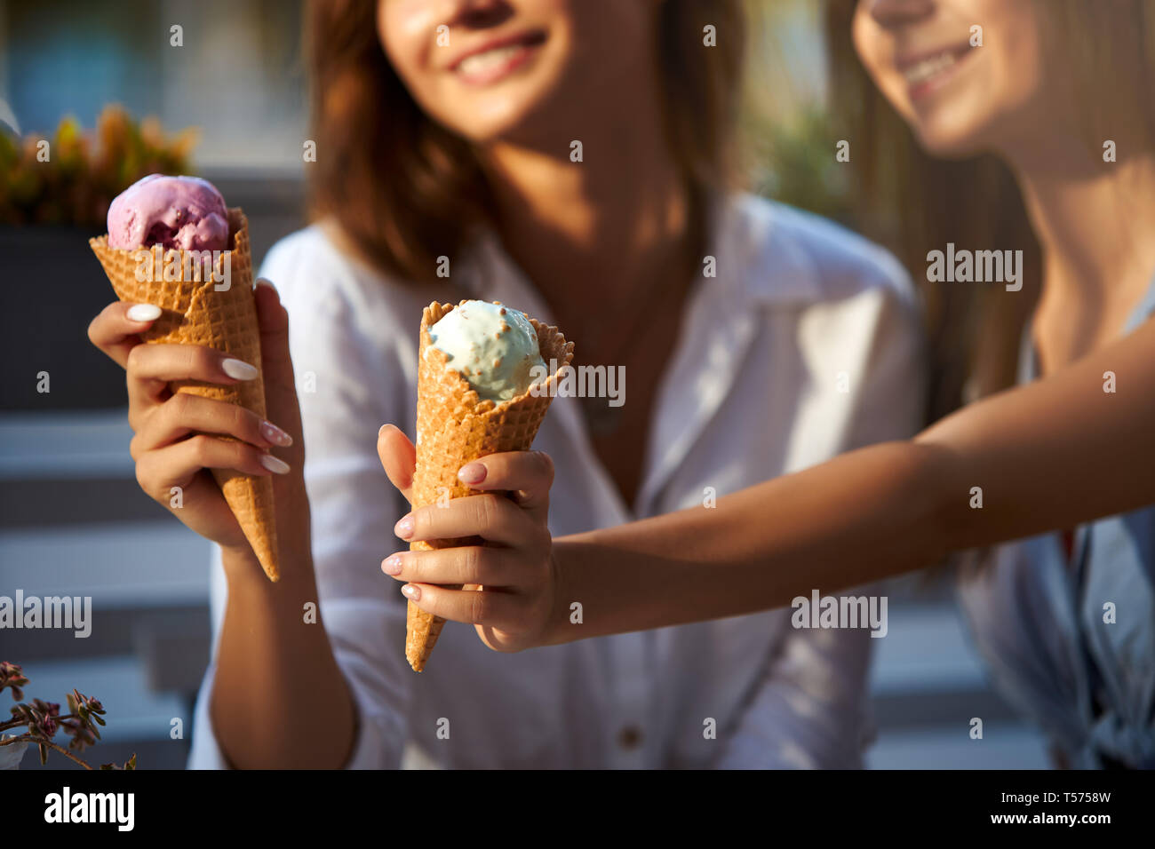 Nahaufnahme von Eistüten in der Hand einer Frau, die mit ihrem Freund. Zwei junge Frauen im Freien essen Eis an einem sonnigen Tag. Isolierte Sicht, Stockfoto