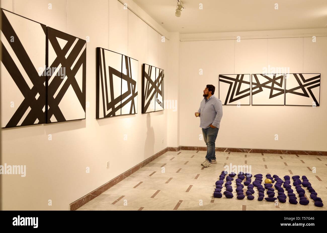 Bagdad, Irak. 20 Apr, 2019. Ein Besucher Gemälde in der Galerie eines irakischen Künstler Zaid al-Ani unter dem Namen ''in einem Saal im Französischen Kulturinstitut in Bagdad, Irak, 20. April 2019 vorstellen. Al-Ani präsentiert eine Sammlung von Gemälden von geometrischen Formen in Schwarz und Weiß, in der er die menschliche Gestalt in einer Weise, die sieht aus wie ein Gravieren einer sumerischen Dichtung verwendet. Gehen mit 'Feature: Auferstanden aus der Asche des Konflikts, der irakische Künstler Kampf für eine bessere Zukunft" Credit: Khalil Dawood/Xinhua/Alamy leben Nachrichten Stockfoto