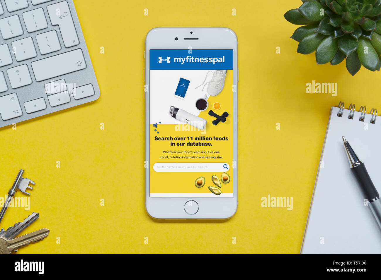 Ein iPhone mit der myfitnesspal Website ruht auf einem gelben Hintergrund Tabelle mit einer Tastatur, Tasten, Notepad und Anlage (nur redaktionelle Nutzung). Stockfoto