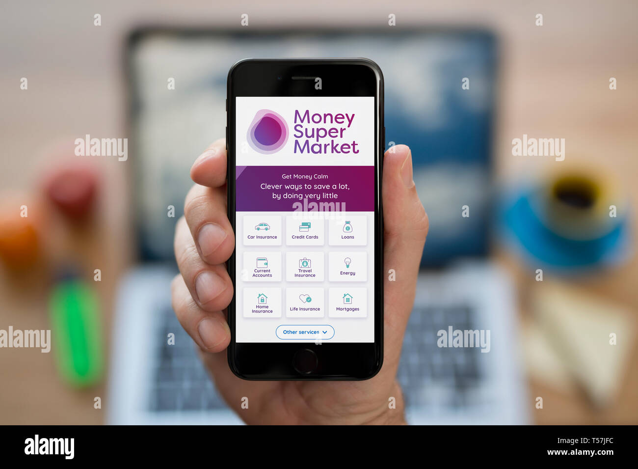 Ein Mann schaut auf seinem iPhone. Das Geld Supermarkt Logo (nur redaktionelle Nutzung). Stockfoto