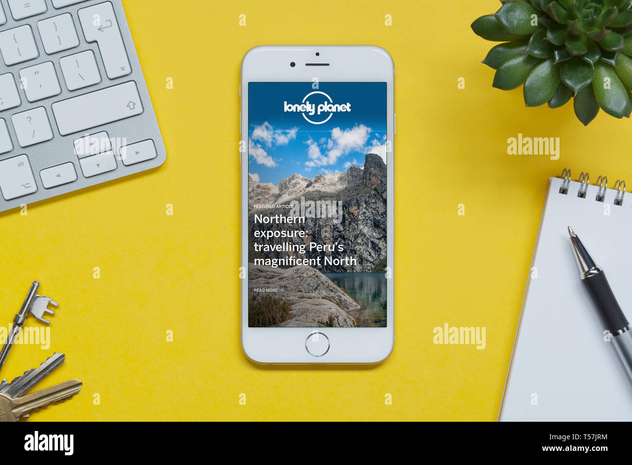 Ein iPhone mit dem Lonely Planet website ruht auf einem gelben Hintergrund Tabelle mit einer Tastatur, Tasten, Notepad und Anlage (nur redaktionelle Nutzung). Stockfoto