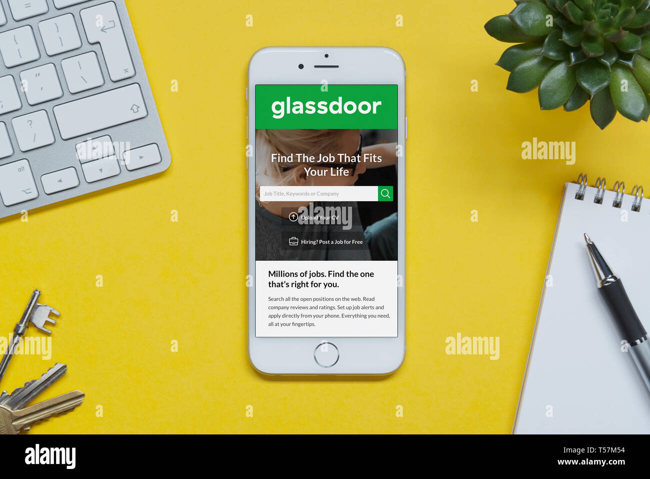 Ein iPhone mit der Glassdoor website ruht auf einem gelben Hintergrund Tabelle mit einer Tastatur, Tasten, Notepad und Anlage (nur redaktionelle Nutzung). Stockfoto
