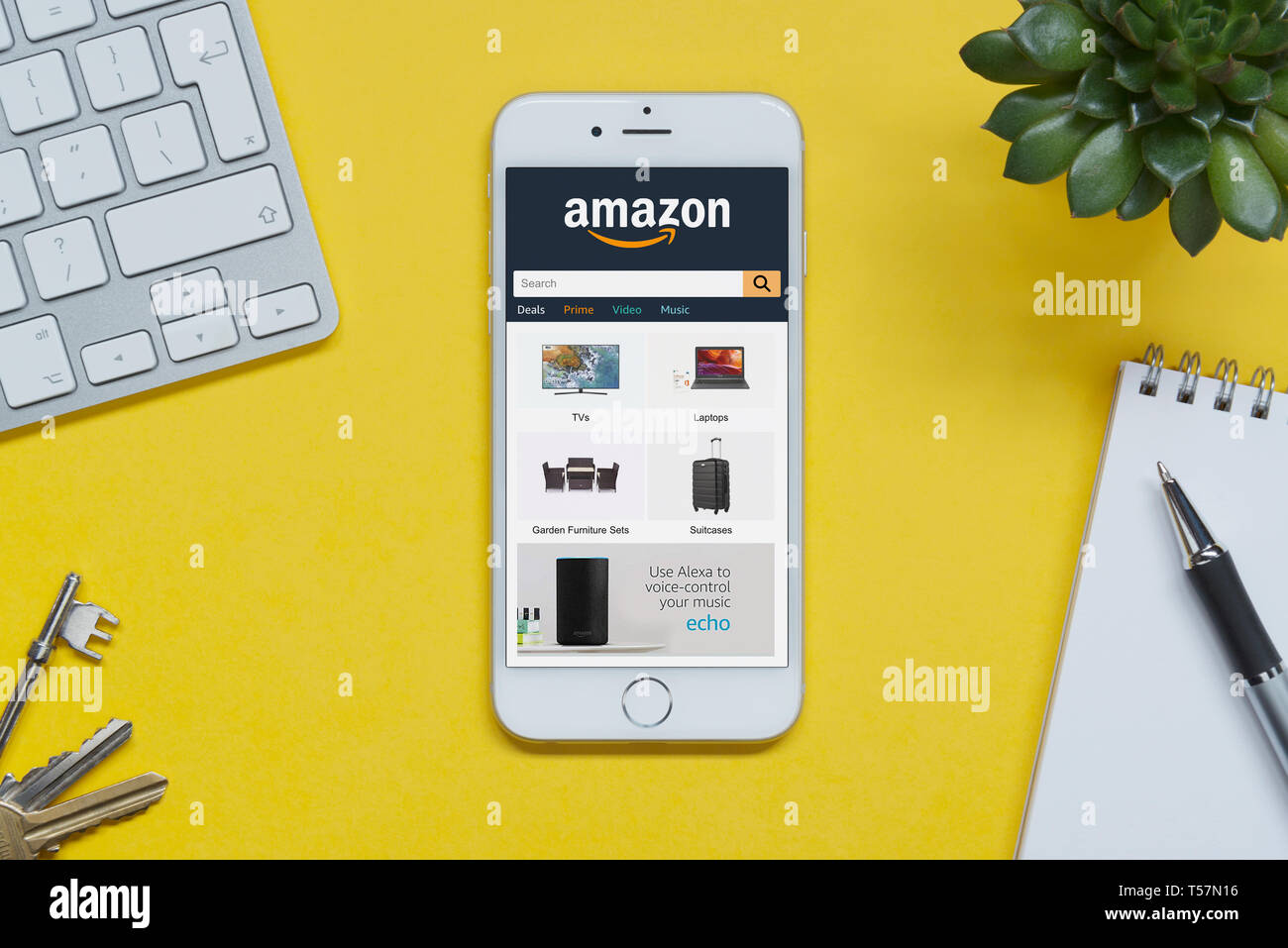 Ein iPhone zeigt die Amazon Website ruht auf einem gelben Hintergrund Tabelle mit einer Tastatur, Tasten, Notepad und Anlage (nur redaktionelle Nutzung). Stockfoto