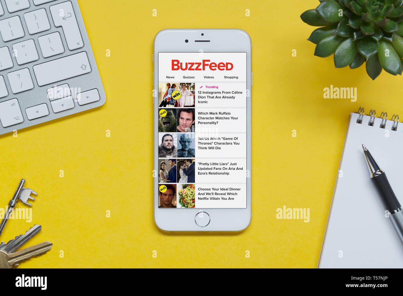 Ein iPhone zeigt die Buzzfeed website ruht auf einem gelben Hintergrund Tabelle mit einer Tastatur, Tasten, Notepad und Anlage (nur redaktionelle Nutzung). Stockfoto