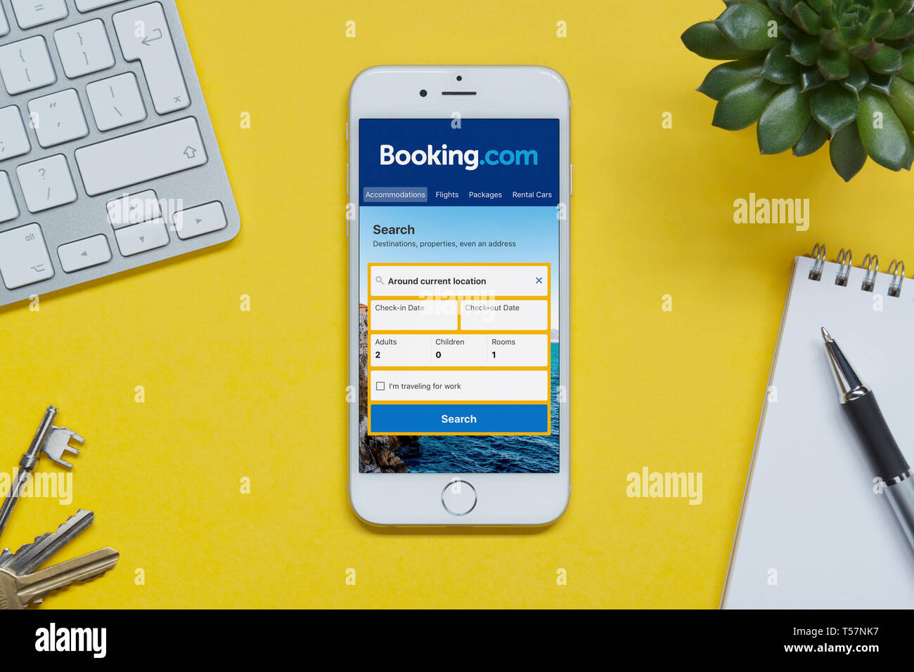 Ein iPhone zeigt die Booking.com Webseite ruht auf einem gelben Hintergrund Tabelle mit einer Tastatur, Tasten, Notepad und Anlage (nur redaktionelle Nutzung). Stockfoto