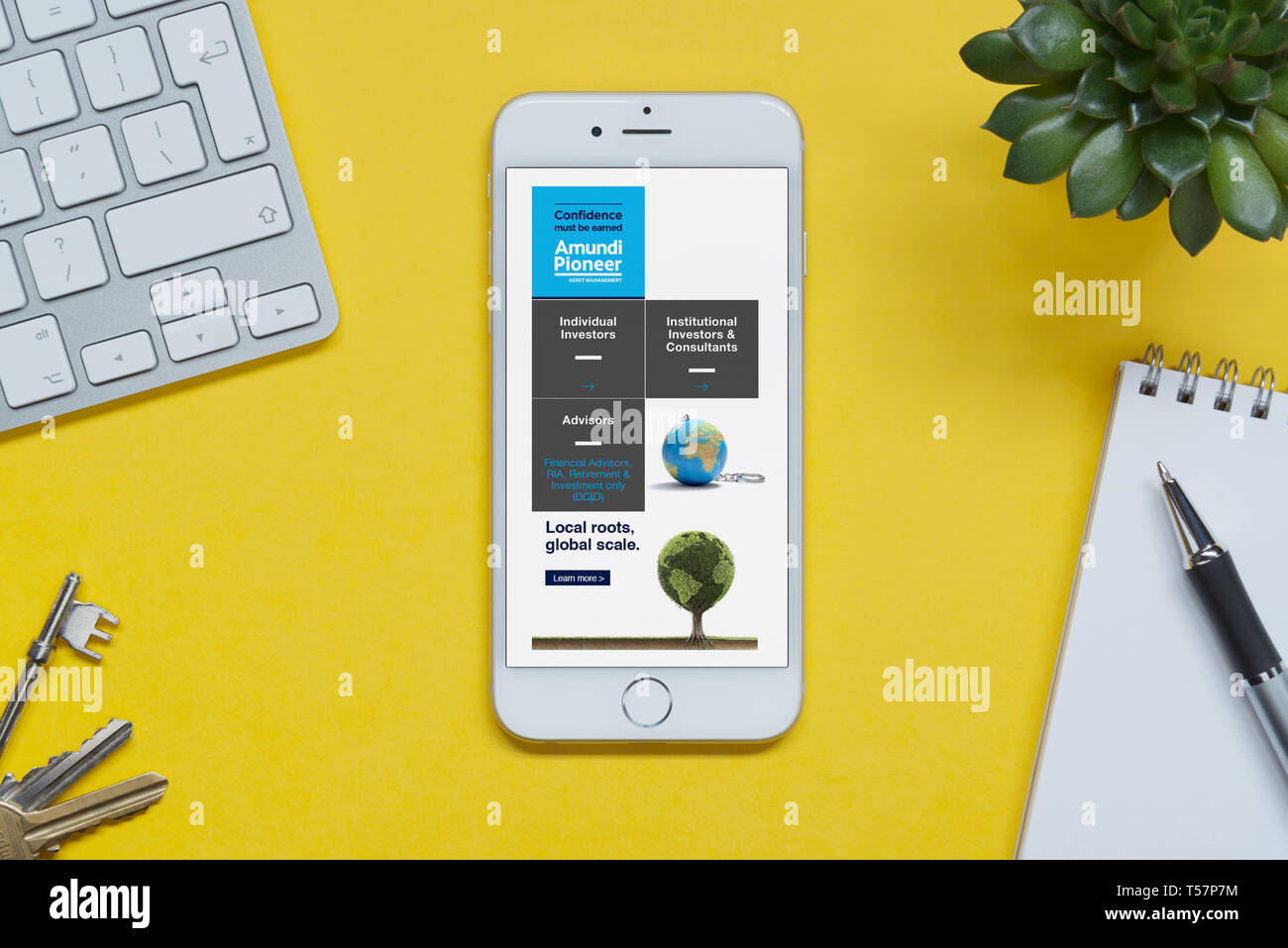 Ein iPhone mit der amundi Asset Management website ruht auf einem gelben Hintergrund Tabelle mit einer Tastatur, Tasten, Notepad und Anlage (nur redaktionelle Nutzung) Stockfoto