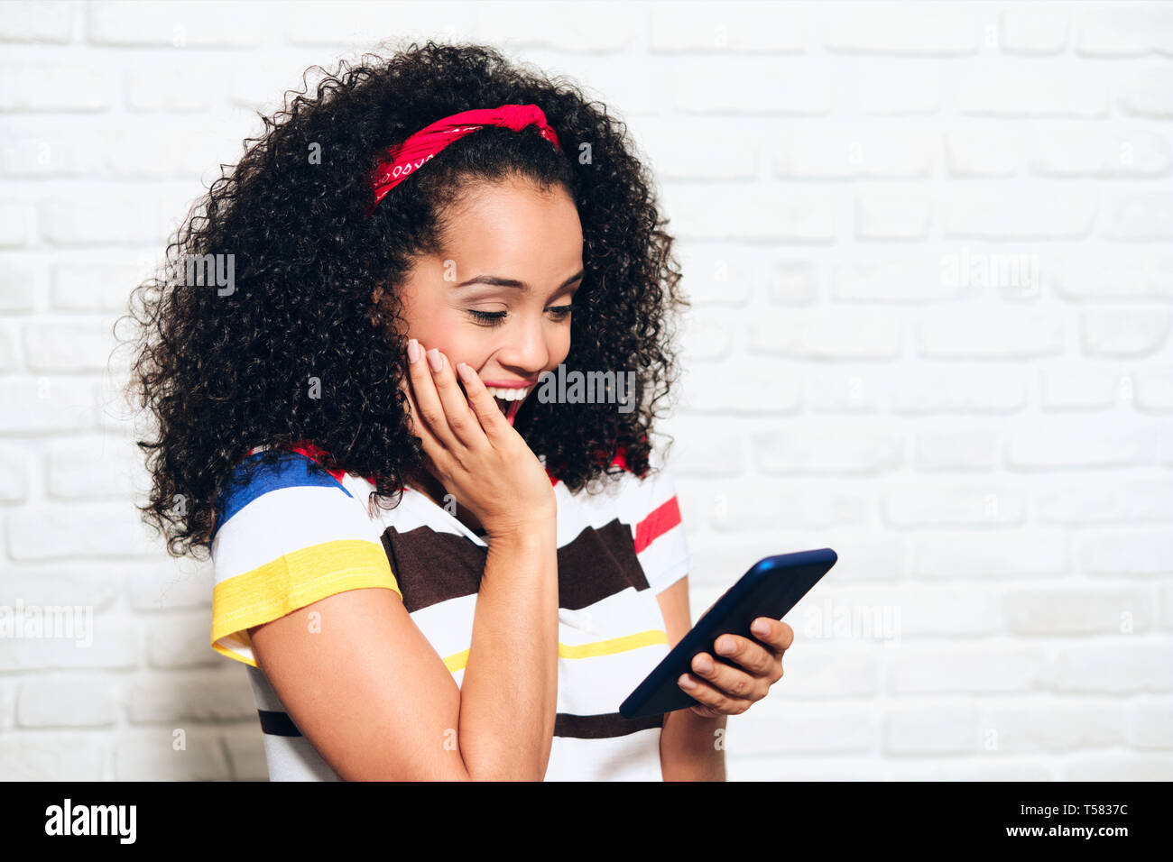 Happy african american woman reading gute Nachrichten auf Handy. Schwarze Mädchen zeigen, Freude und Glück für die Anzeige auf mobilen Telefon. Hispanische person wi Stockfoto