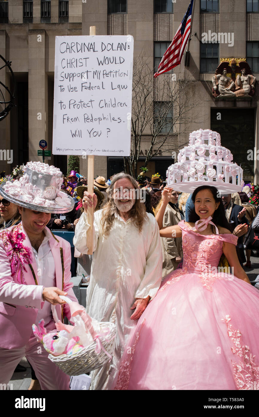 New York, NY - 21. April 2019. Ein paar mit verzierten Hochzeit - Kuchen Hüte neben einem Mann mit einem Schild bittet Kardinal Dolan Kinder aus pedop zu schützen. Stockfoto