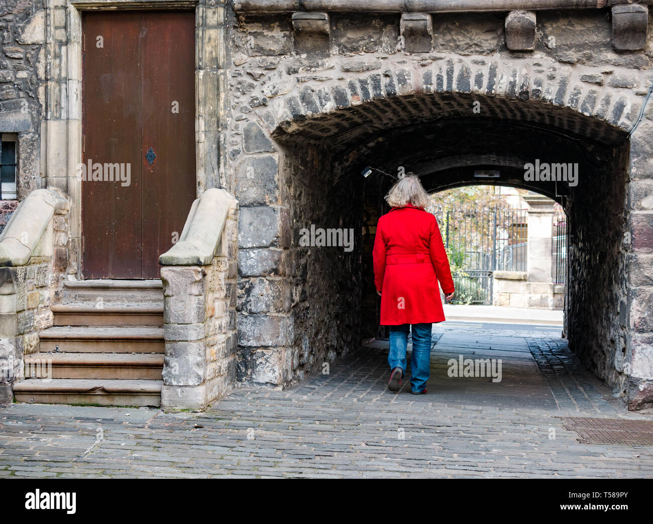 Ältere Frau mit roten Mantel zu Fuß durch gewölbte enge Passage, Backstube, in der Nähe der Royal Mile, Edinburgh, Schottland, Großbritannien Stockfoto