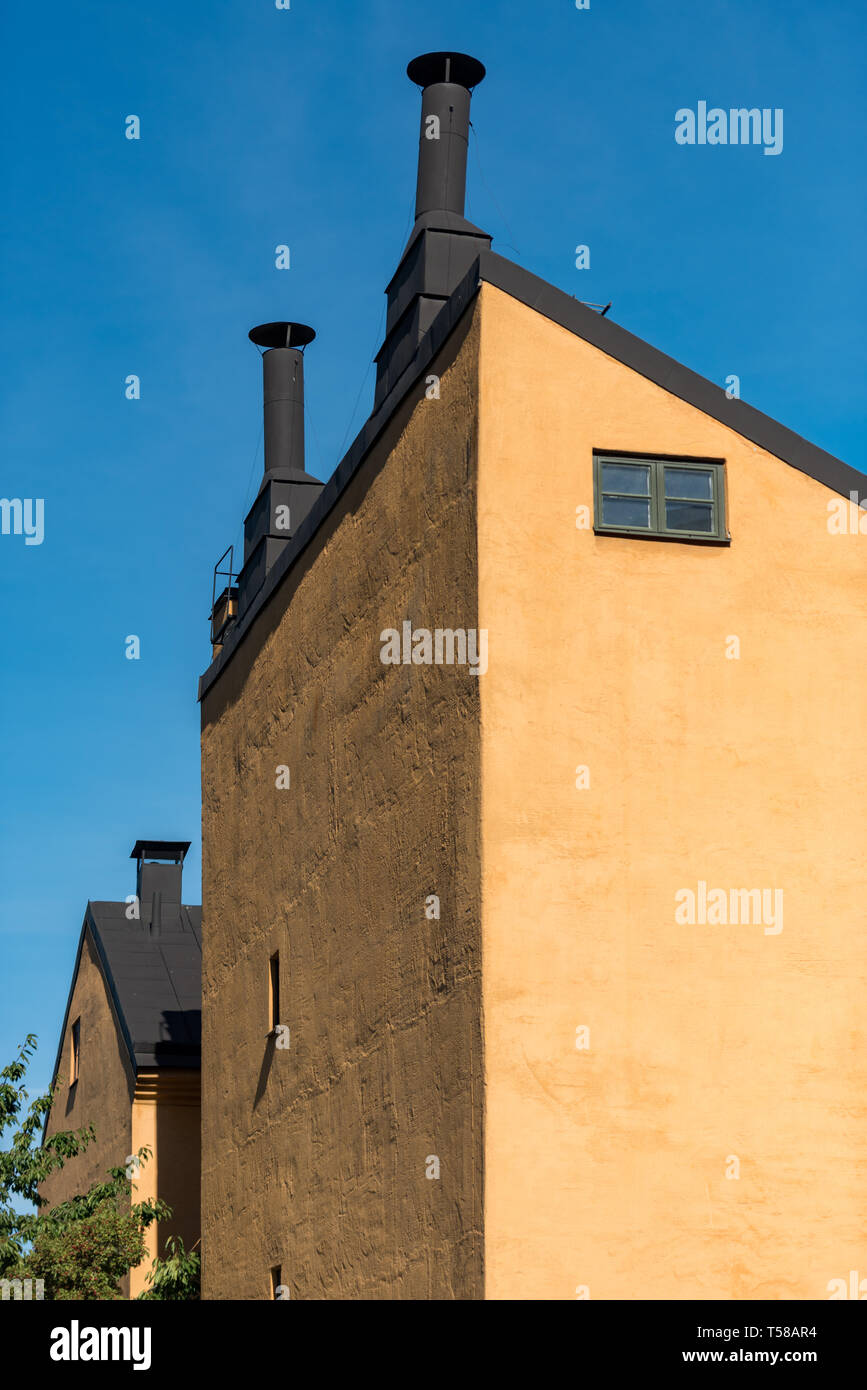 Markante schwarze Schornsteine Krone einen hellen ockerfarbenen Gebäudes vor einem tiefblauen Himmel in Södermalm Bastugata Stockfoto