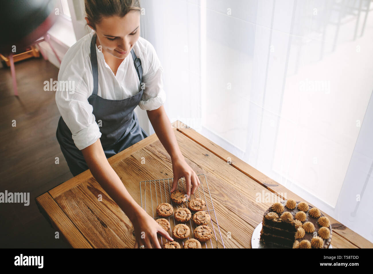 Blick von oben auf die weiblichen Konditor cookies Vorbereitung in der Küche. Frau Baker, die die Cookies auf dem Grill mit einem Kuchen auf dem Tisch. Stockfoto
