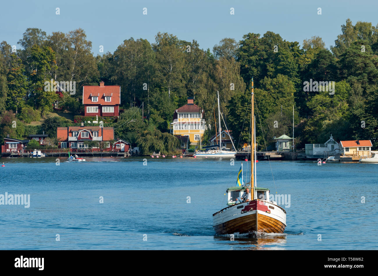 Ein Fischerboot übergibt einen Weiler der traditionellen bunten Holzhäusern auf Skarpö in den Stockholmer Schären. Stockfoto