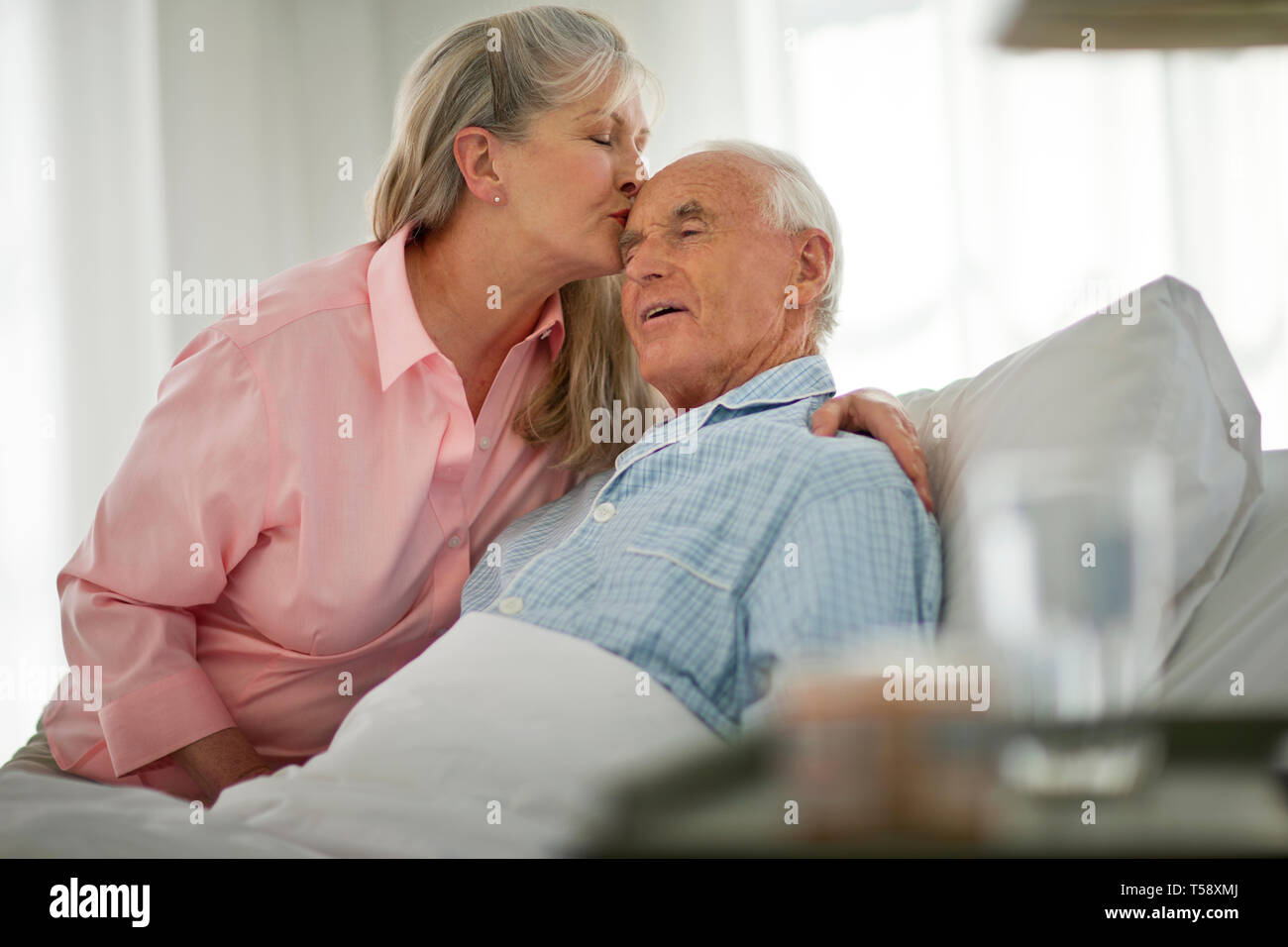 Älterer Mann küsste auf der Stirn von seiner Frau, als er im Bett liegt. Stockfoto
