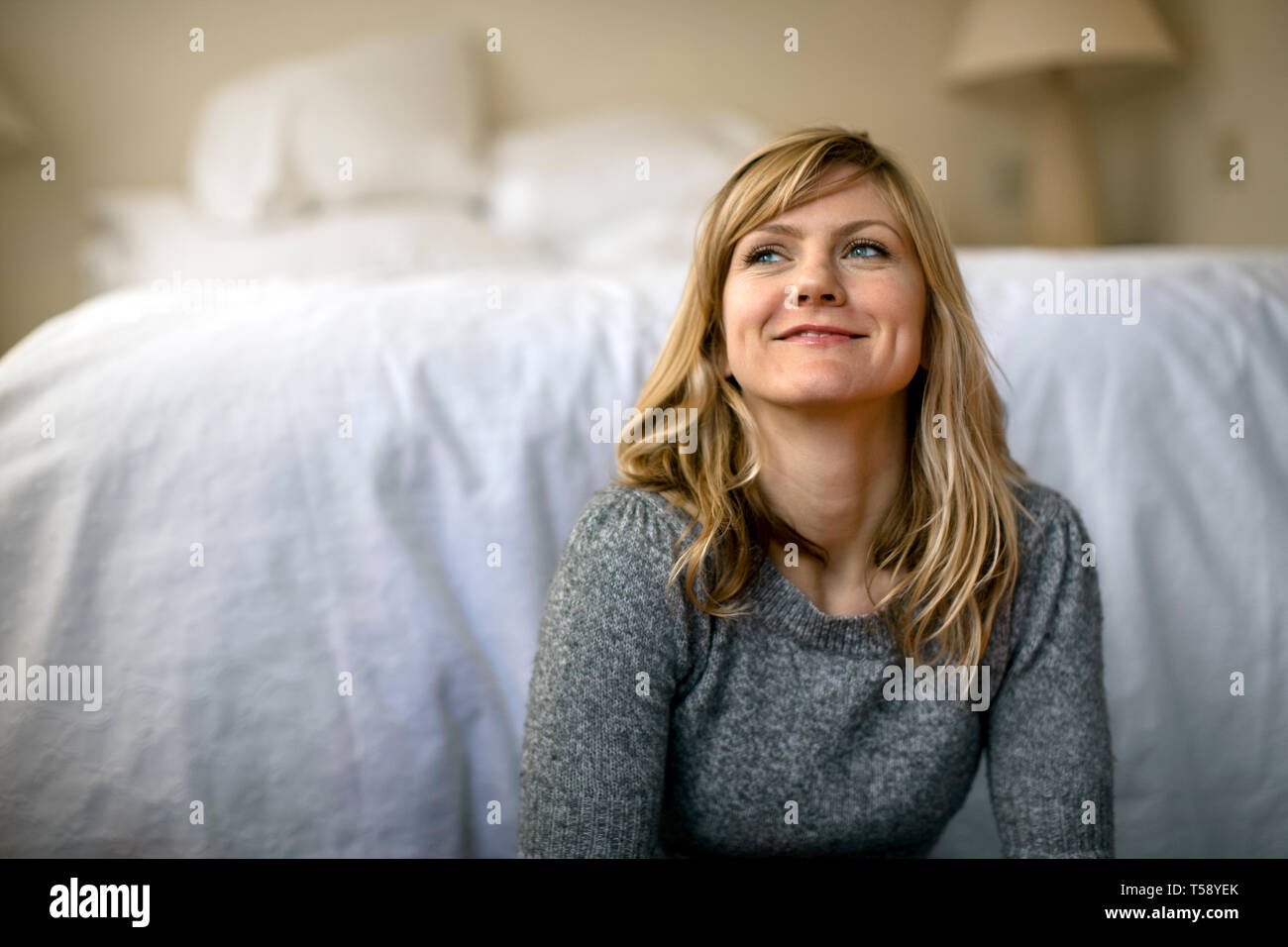 Junge Frau lächelt glücklich in der Ferne, als sie sitzt und Tagträume auf dem Fußboden ihres Schlafzimmers. Stockfoto